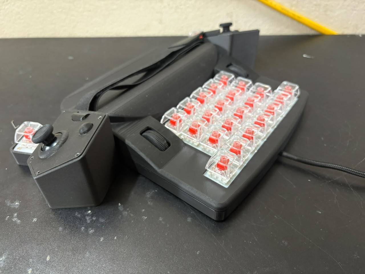 Angled view of the ERCHAM MK1 functional prototype showing clear red mechanical switches, the side scroll wheel, and a detached thumb cluster with analog stick